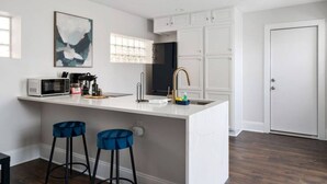 Een moderne keuken met een wit kookeiland, barkrukken, een magnetron en een koffiezetapparaat.