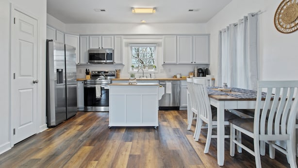 Una cocina moderna con muebles blancos, electrodomésticos de acero inoxidable, una isla central y un comedor con sillas blancas.