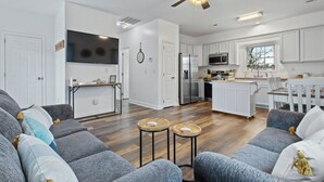 Una cocina moderna con armarios blancos, una isla central y un comedor con una mesa y sillas blancas.
