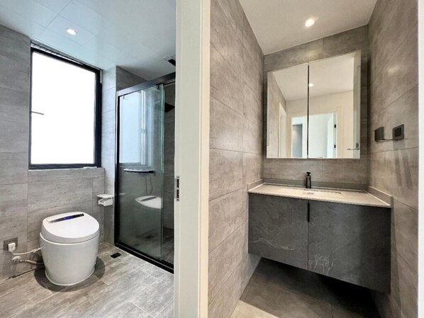 Un baño moderno con cabina de ducha de vidrio, inodoro blanco y tocador con espejo.