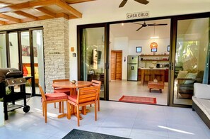 A modern kitchen with a refrigerator, a dining area with a table and chairs, and a grill outside.