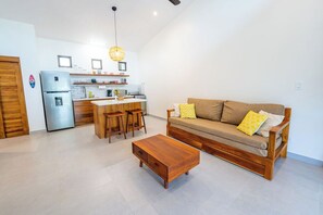 A modern living room with a sofa, coffee table, and kitchen area with a refrigerator and bar stools. - Serene and Tropical Villa w/Pool - Casa Cielo, Playa Pelada (NICOYA)