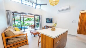 Ein modernes Wohnzimmer mit einer Couch, einem Holztisch, einem Fernseher und einer großen Schiebeglastür, die auf eine Terrasse führt.