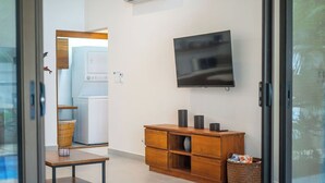 Una sala moderna con un televisor de pantalla plana montado en la pared, un mueble de madera con cajones, una cesta de mimbre y una pequeña mesa.