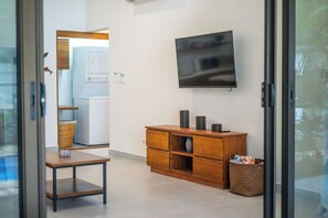 A modern living room with a flat-screen TV mounted on the wall, a wooden cabinet with drawers, a wicker basket, and a small table. - Peaceful Tropical Villa w/ Pool and Walking Distance to Beach- Casa Mar Nosara (NICOYA)