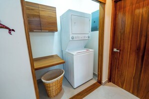 A laundry room with a washing machine and dryer, wooden cabinets, a wicker basket, and a wooden door.