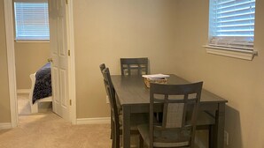 A dining area with a table and chairs, a ceiling fan, and a window with blinds. - Charming 2-bedroom house in Bay St. Louis with WiFi and AC (Bay St. Louis)