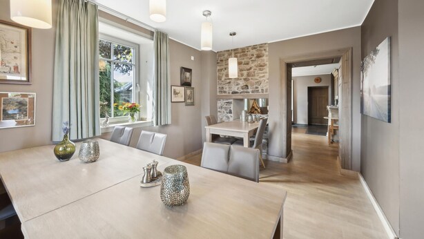 A dining area with a large table, chairs, and decorative items. There is a window with curtains, a stone wall, and a door leading to another room. - Amazing home in Feuerscheid (Feuerscheid)