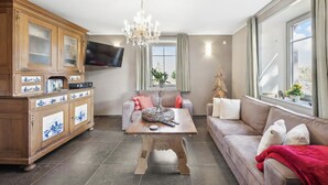A living room with a wooden cabinet, a television, a chandelier, a sofa, and a window with curtains. - Amazing home in Feuerscheid (Feuerscheid)