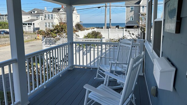 A covered porch with white railings and rocking chairs, overlooking a residential street and ocean view. - Charming 3-bedroom house with ocean views, WiFi, AC in delightful Hull (Hull)