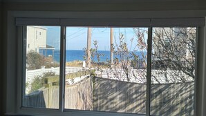 A room with a large window overlooking a wooden fence and a view of the ocean. - Charming 3-bedroom house with ocean views, WiFi, AC in delightful Hull (Hull)