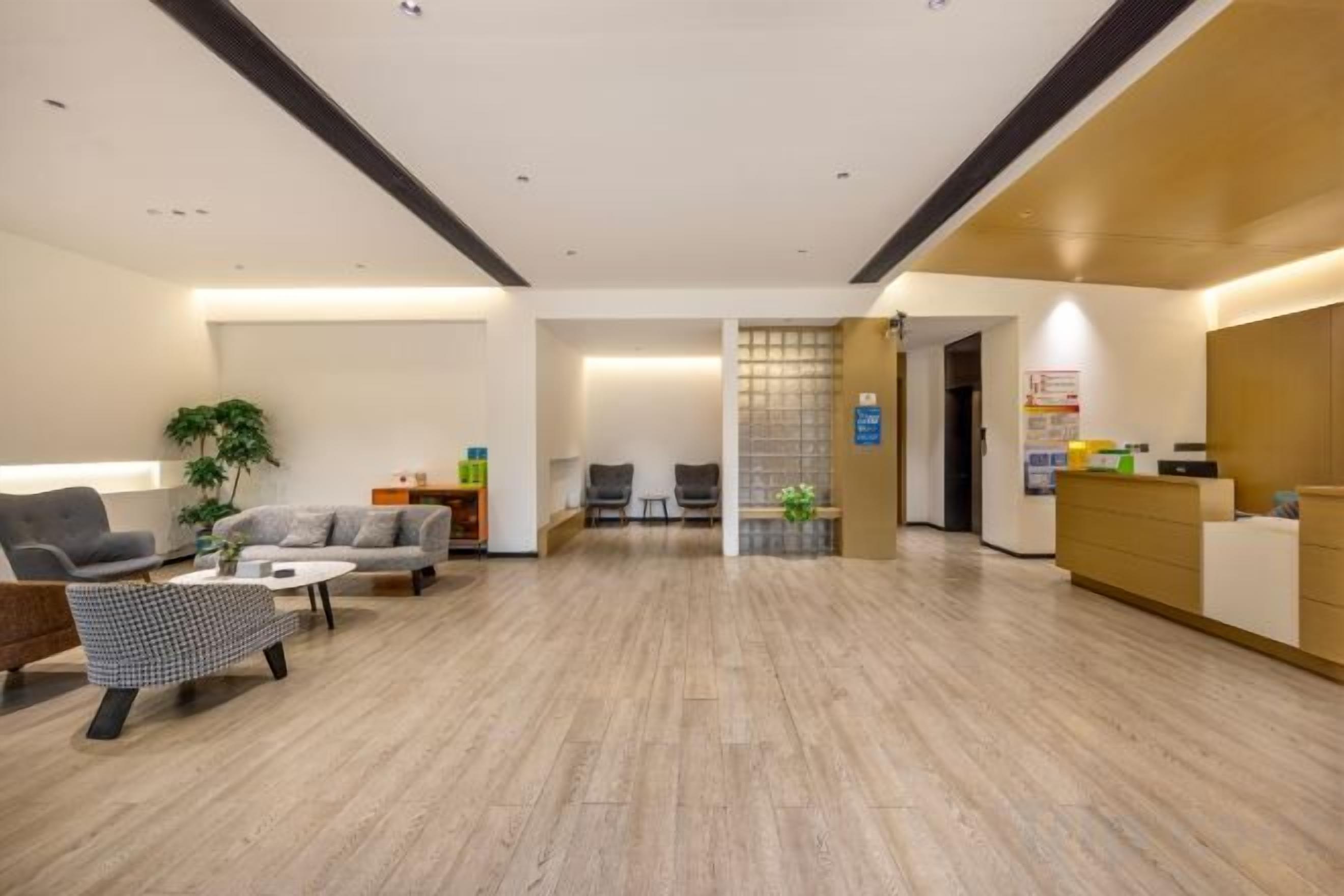A modern hotel lobby with a reception desk, seating area, and a plant.