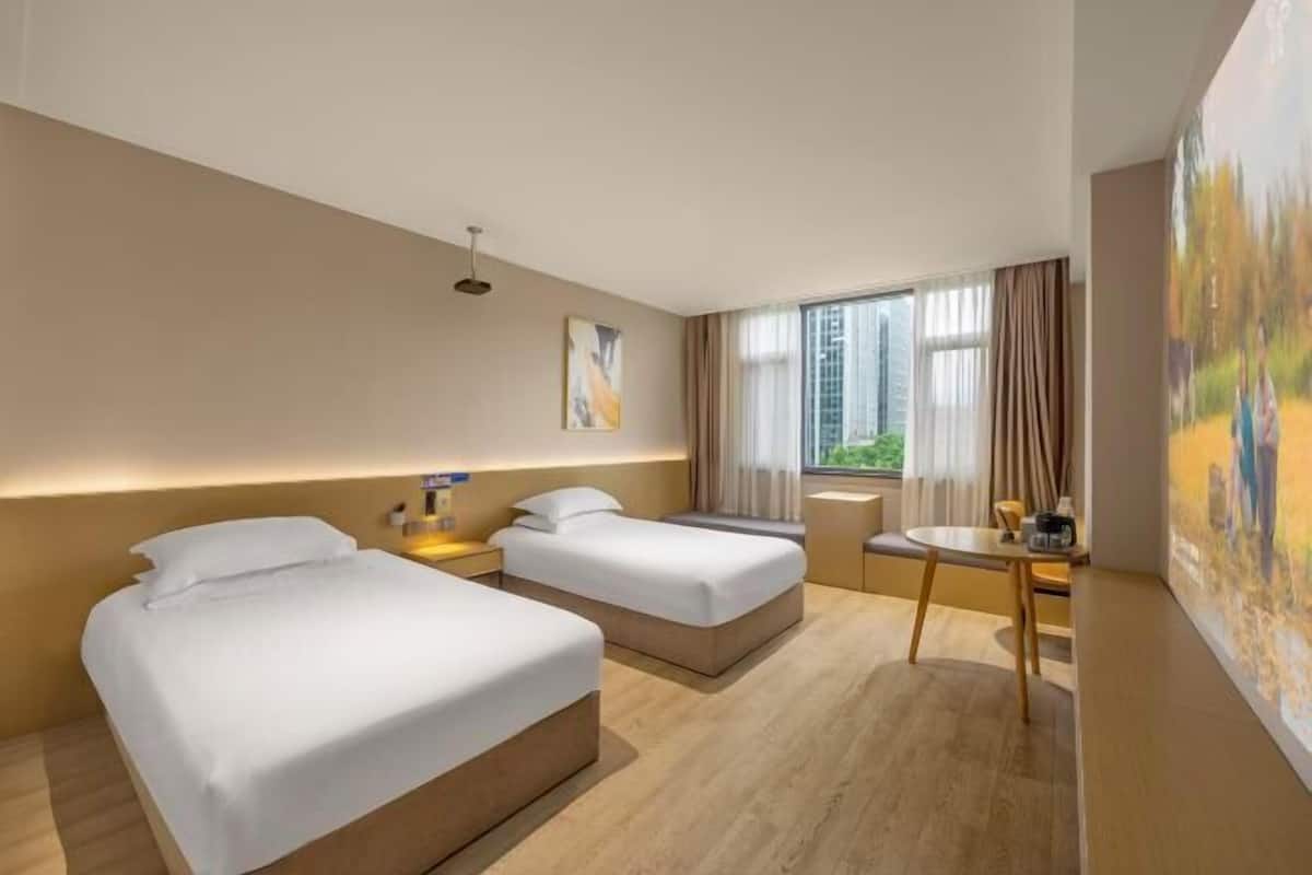 A hotel room with two beds, a desk, and a window with curtains.