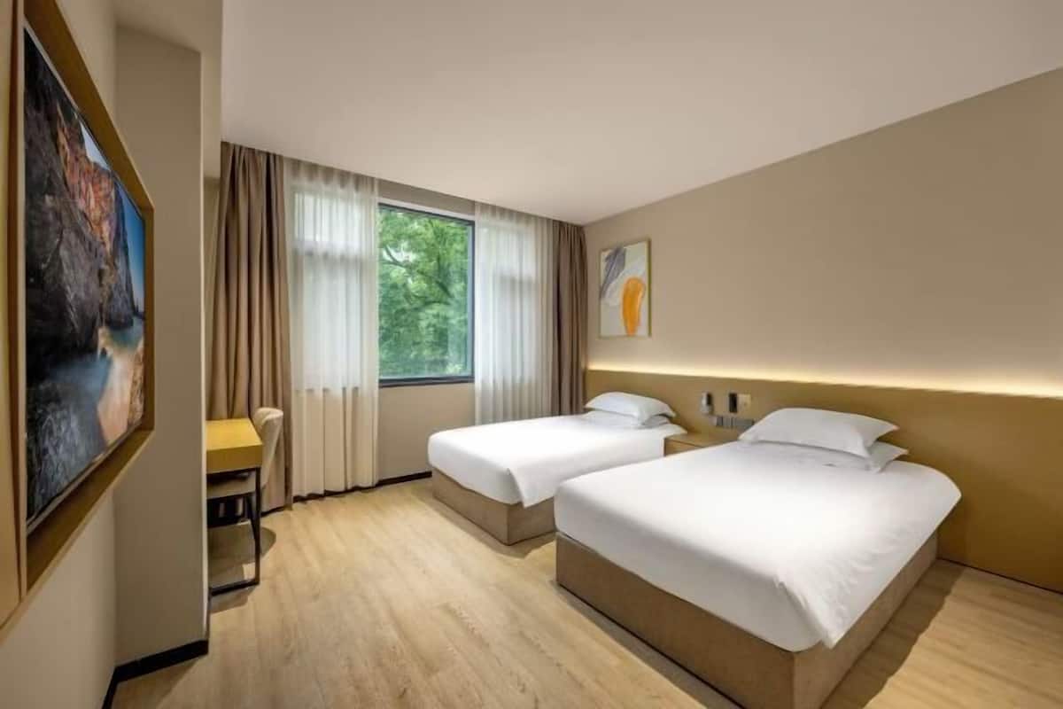 A hotel room with two beds, a desk, a chair, and a large window with curtains.