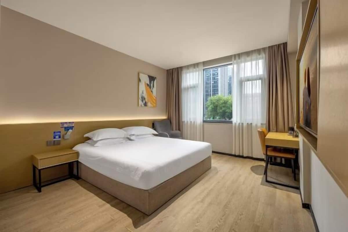 A hotel room with a bed, bedside table, chair, desk, and a window with curtains.