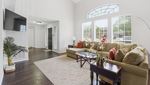 A spacious living room with a large window, a flat-screen TV, a sofa, and a coffee table.