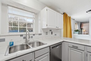 A kitchen with a double sink, white cabinets, a dishwasher, and a window with blinds.