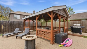 A covered patio area with lounge chairs, a fire pit, and a grill.