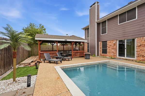 Un jardin avec une piscine, des meubles de patio et un espace salon abrité.