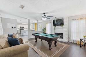 Un salon équipé d’une table de billard, d’un ventilateur de plafond, d’une cheminée et d’un téléviseur fixé au mur.