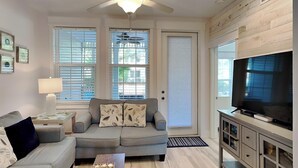 A living room with a grey sofa, a coffee table, a TV on a cabinet, and a ceiling fan. - The Village #611 by Southern Vacation Rentals (Santa Rosa Beach)