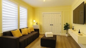 A living room with a sofa, ottoman, and a TV mounted on the wall.