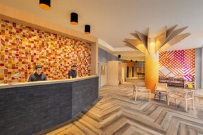 A hotel reception area with a patterned wall, a modern reception desk, and a seating area with chairs and a table. - Ginger Kochi, Kalamassery (Kanayannur)