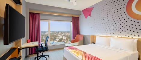 A hotel room with a bed, a desk, a chair, a TV, and a window with curtains.