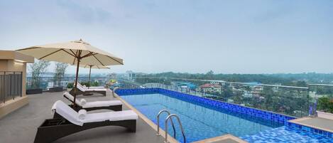 An outdoor infinity pool with lounge chairs and umbrellas, surrounded by a cityscape view.
