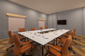 A conference room with a long table, orange chairs, a flat-screen TV, and a projector screen on the wall. - Ginger Kochi, Kalamassery (Kanayannur)