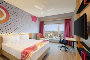 A hotel room with a large bed, a desk, a chair, a TV, and a view of the city. - Ginger Kochi, Kalamassery (Kanayannur)