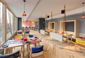 A modern restaurant with wooden flooring, multiple tables and chairs, hanging pendant lights, and large windows. - Ginger Kochi, Kalamassery (Kanayannur)