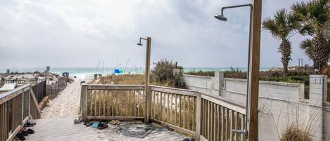 Un muelle de madera que conduce a una playa, con barandilla de metal y un rociador.