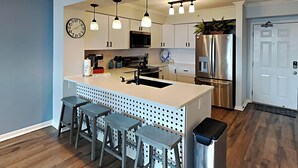 Une cuisine moderne dotée d’un îlot central, de tabourets de bar, d’appareils électroménagers en acier inoxydable et de luminaires suspendus.
