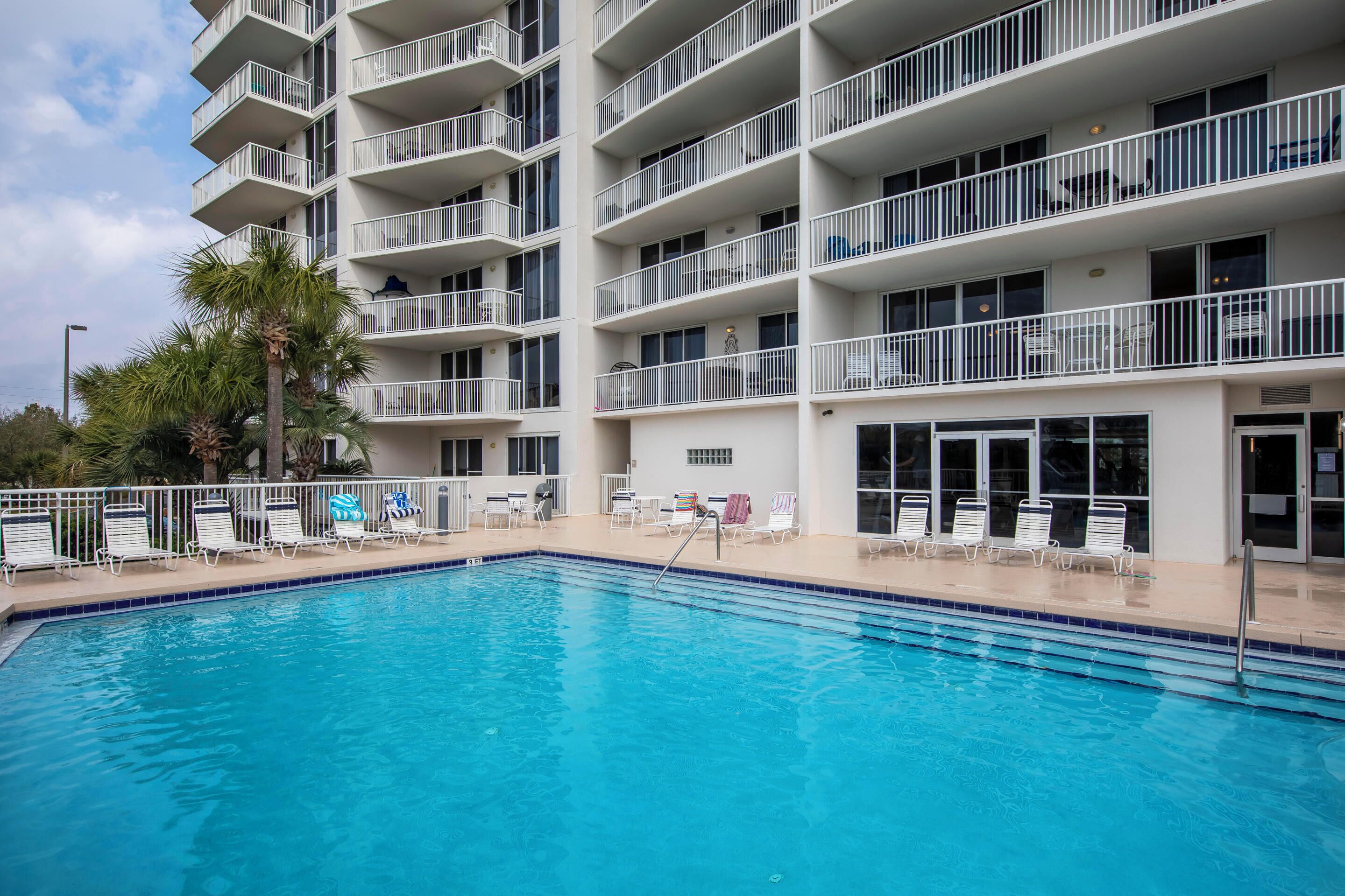 A swimming pool with lounge chairs and a multi-story building with balconies.