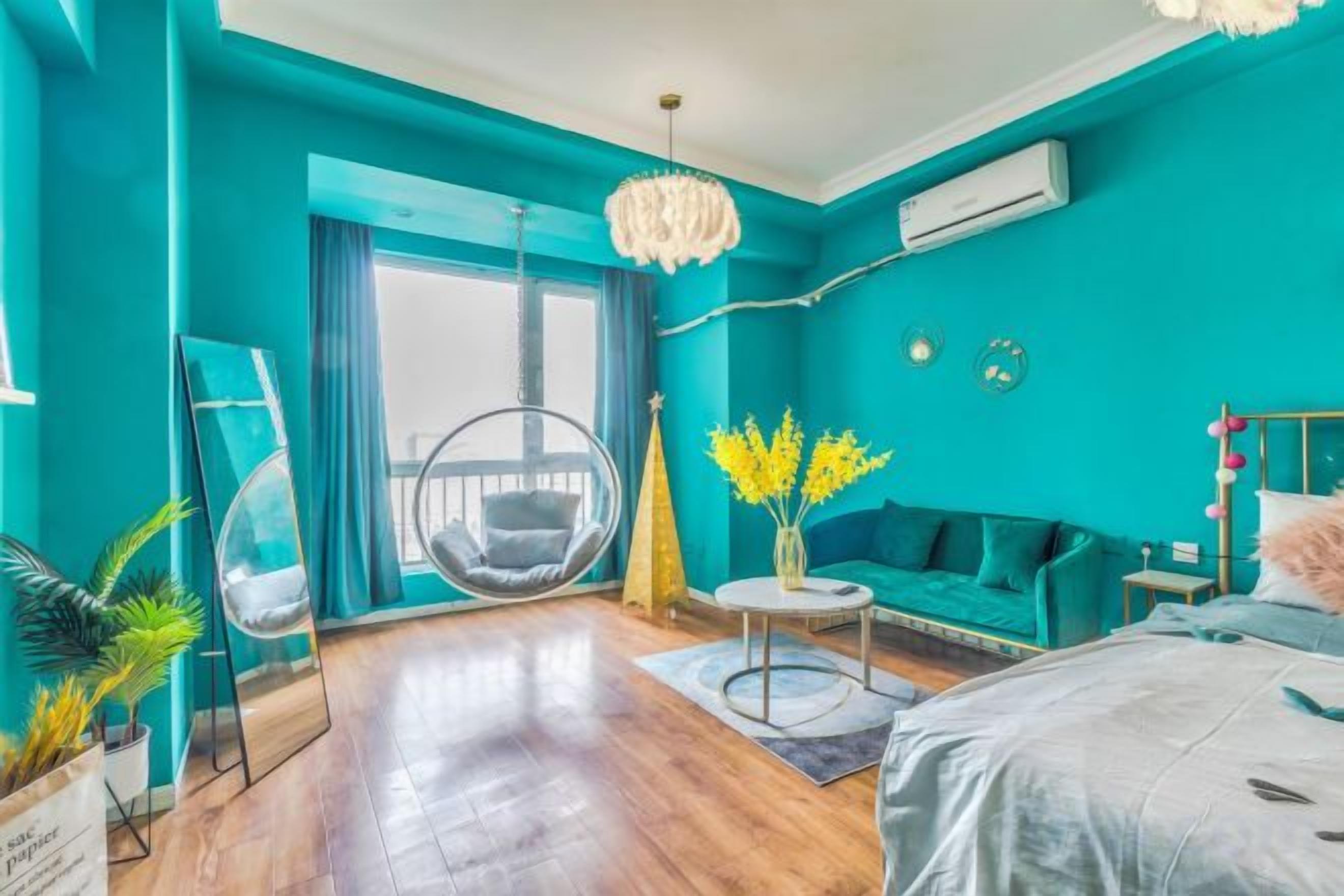 A teal-themed room with a hanging chair, a sofa, a small round table, and a bed.