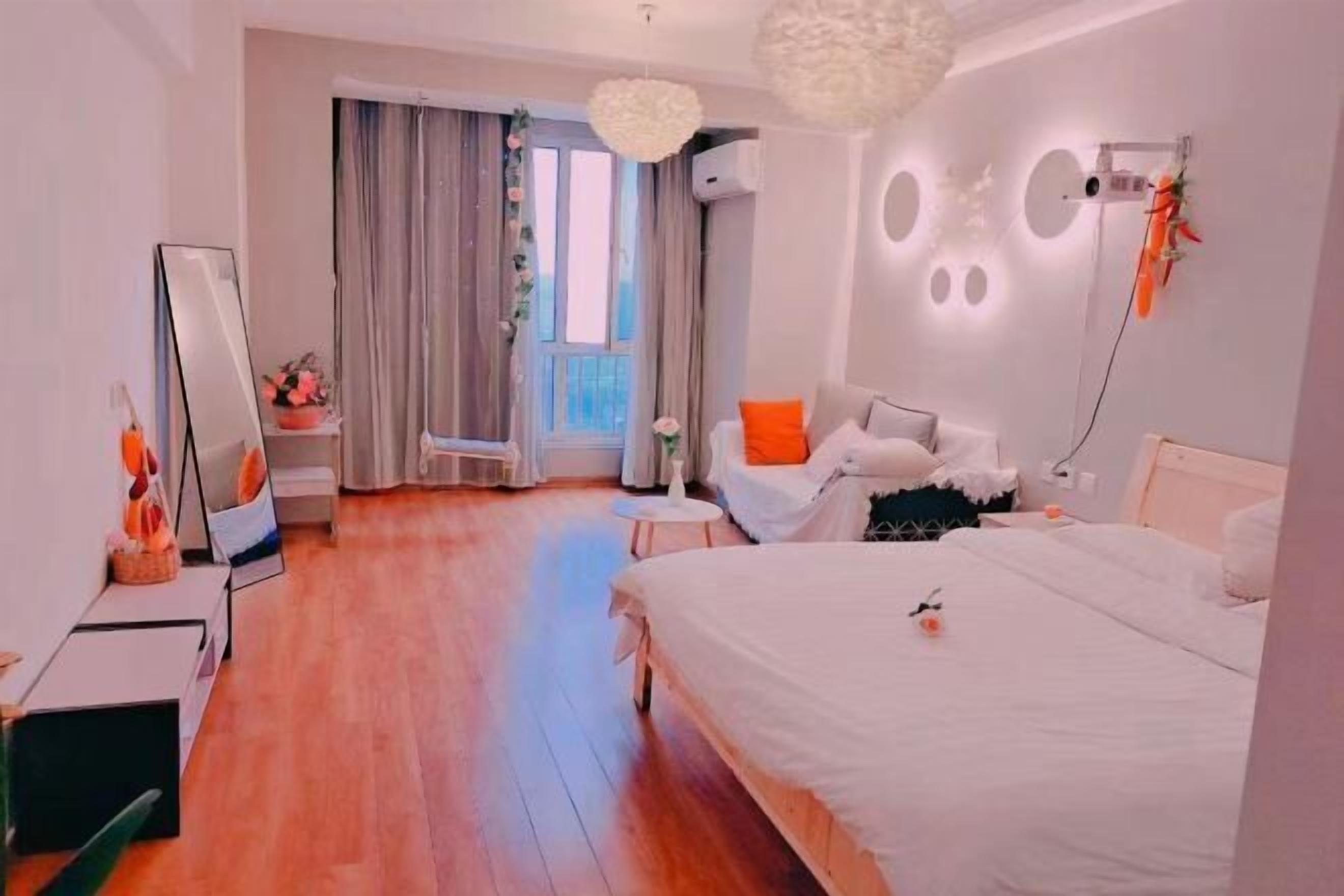 A modern bedroom with a large bed, a seating area, a mirror, and a window with curtains.