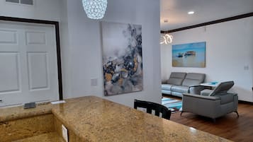 Uma sala de estar moderna com um sofá cinza, uma mesa de centro e uma pintura de barcos na parede.