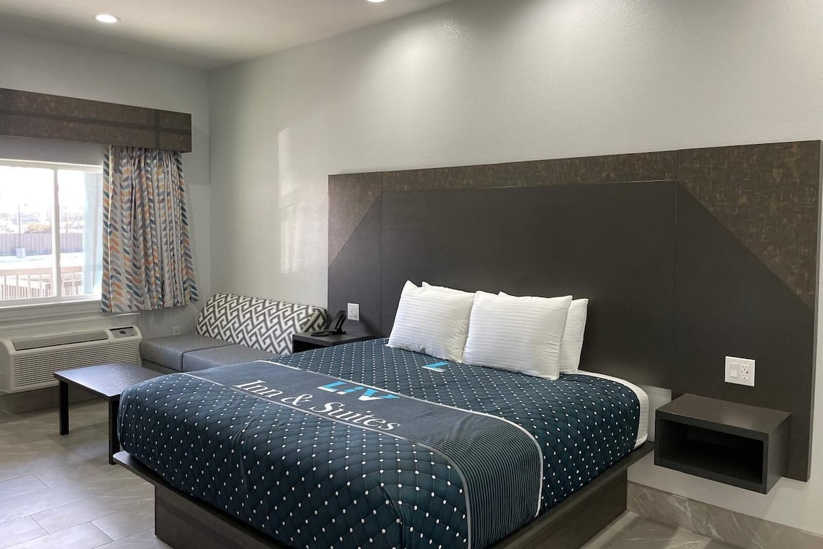 Quarto de hotel moderno com uma cama grande, mesa de cabeceira, prateleira embutida e uma janela com cortinas.