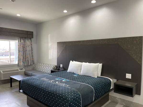 A modern hotel room with a large bed, a bedside table, a built-in shelf, and a window with curtains. - Liv Inn and Suites (Houston)