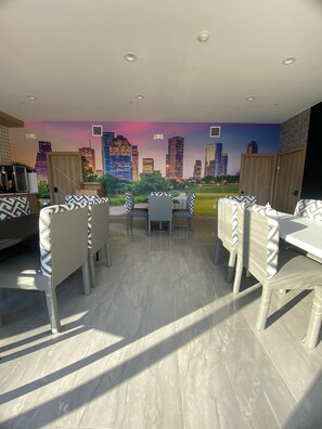 Un área de comedor con un mural de paisaje urbano, muebles modernos y piso de baldosas.