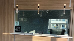 Ein Empfangstresen mit Schild zur Anzeige der Check-in- und Check-out-Zeiten, ein Dell-Laptop und Blick auf ein Gebäude im Freien.