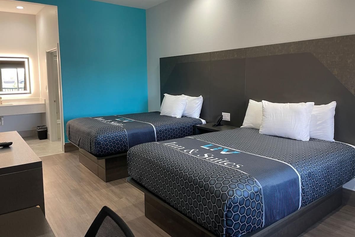 Quarto de hotel com duas camas, uma escrivaninha e uma janela.