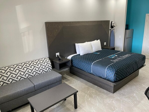 Una habitación de hotel moderna con una cama grande, un sofá, una mesita y una mesita de noche.