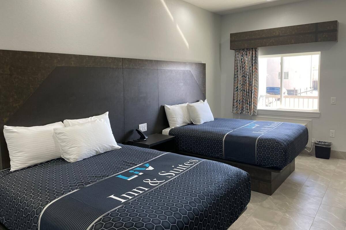 Quarto de hotel com duas camas, cabeceira escura, janela com cortinas e vista para o exterior.