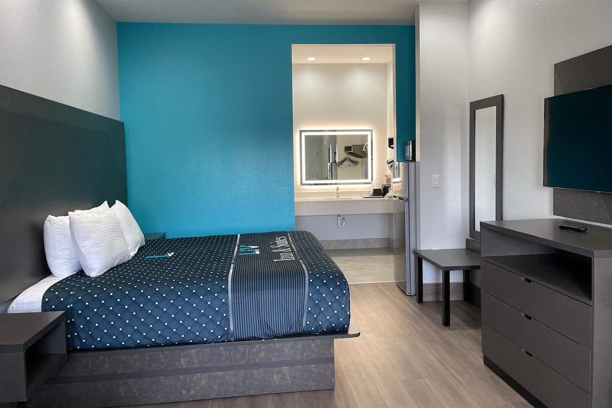 Quarto de hotel moderno com uma cama, toucador com espelho, televisão e secretária.