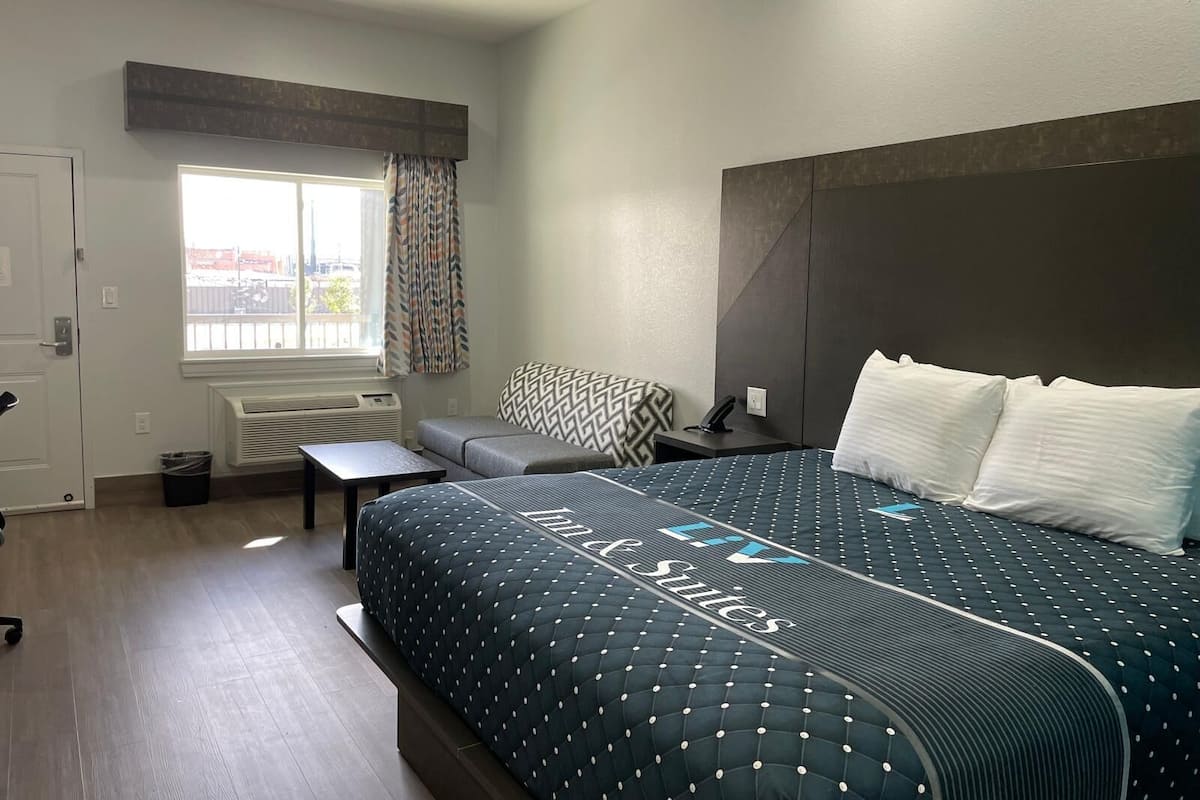 Quarto de hotel com uma cama grande, uma escrivaninha, uma cadeira, uma janela com cortinas e um radiador.