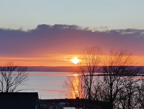 Auringonlasku vesistön yllä, etualalla paljaita puita.