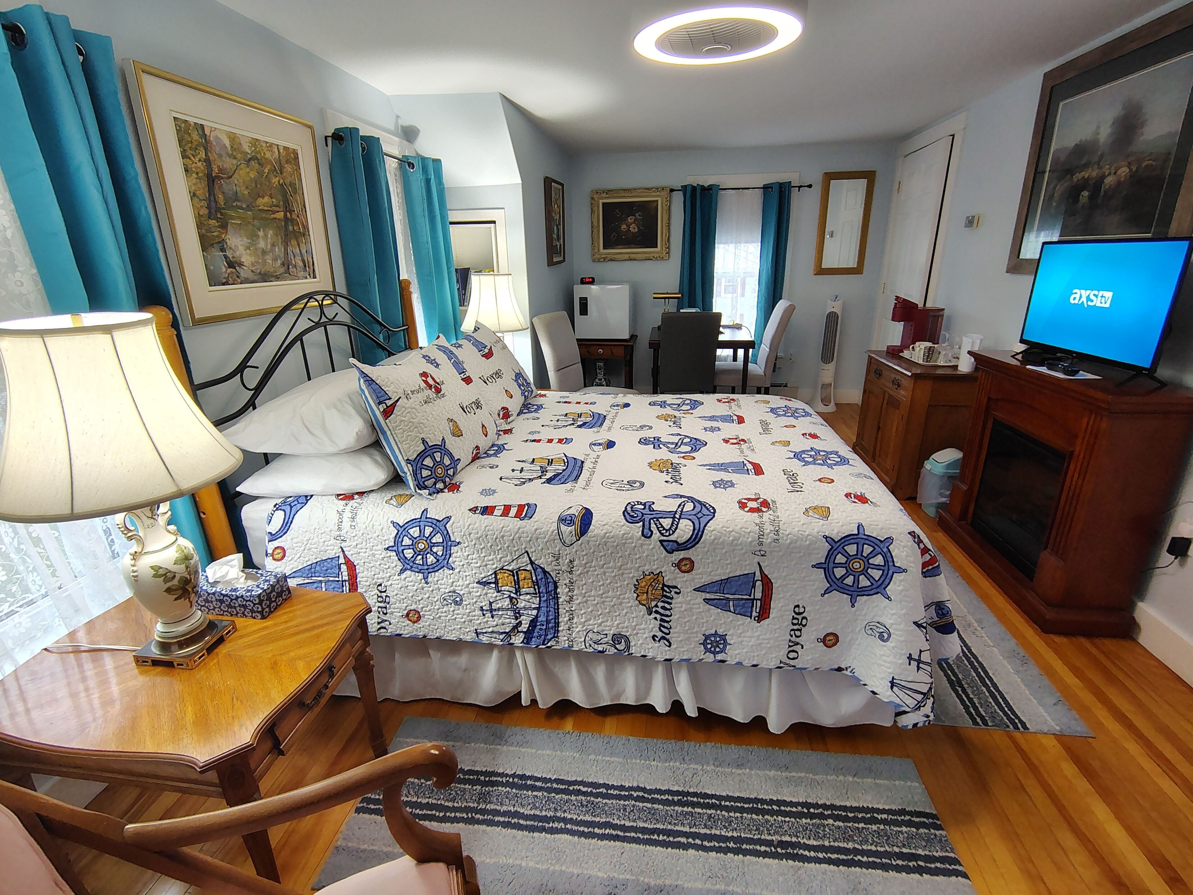 A hotel room with a bed, a desk, a chair, a TV, and a fireplace.