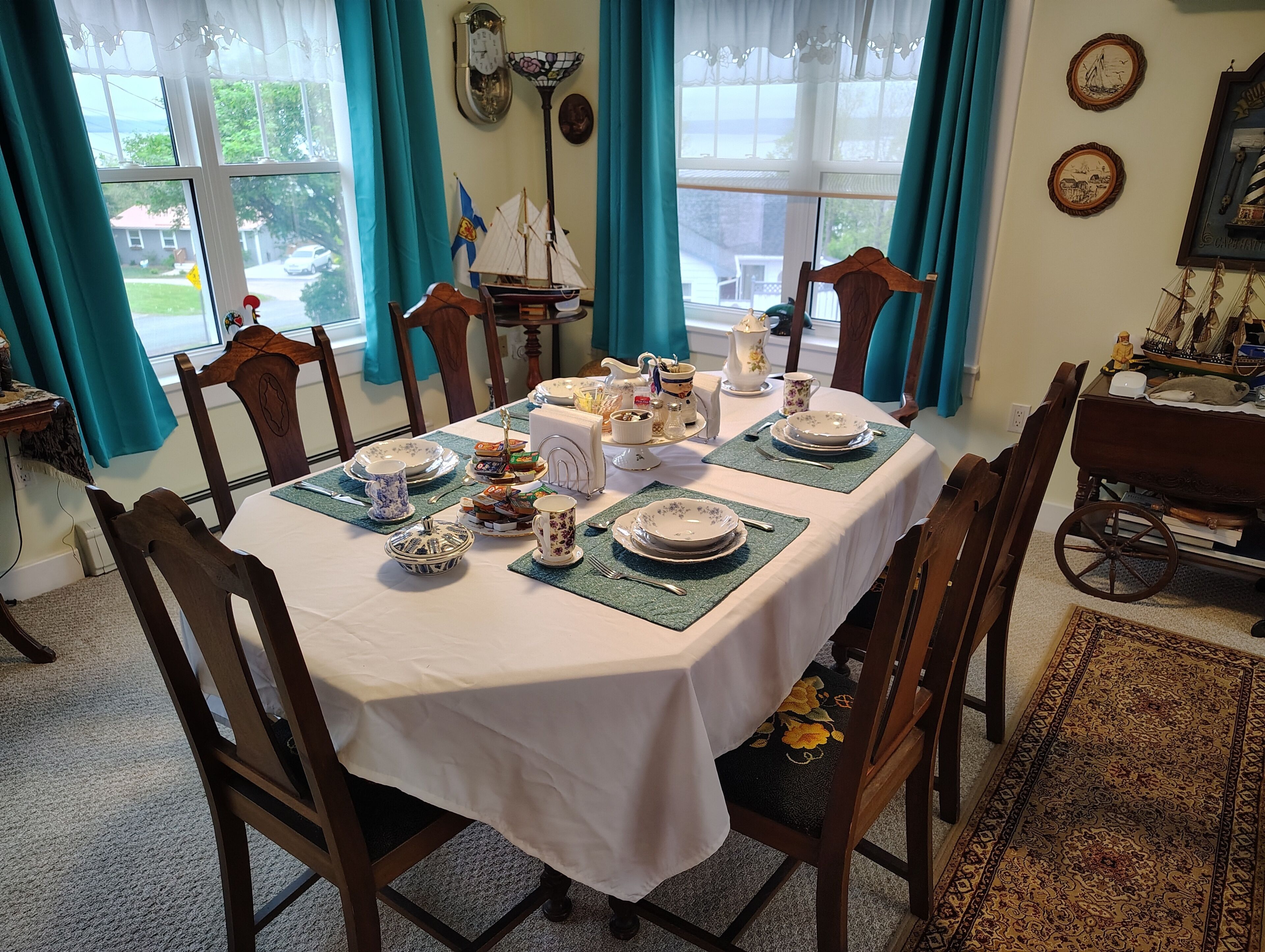 A dining room with a table set for four, chairs, a clock, and a window with curtains.
